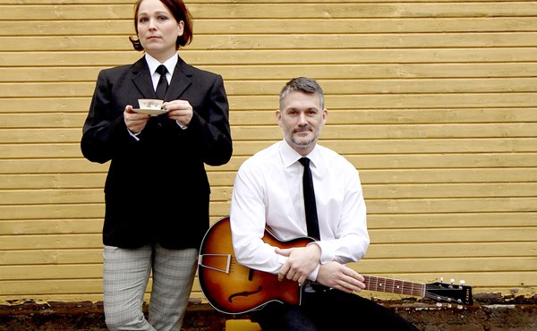 Två musiker iklädd Beatles kostym poserar med gitarr och tekopp