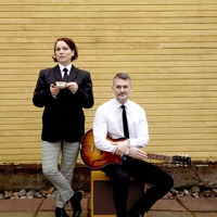 Två musiker iklädd Beatles kostym poserar med gitarr och tekopp