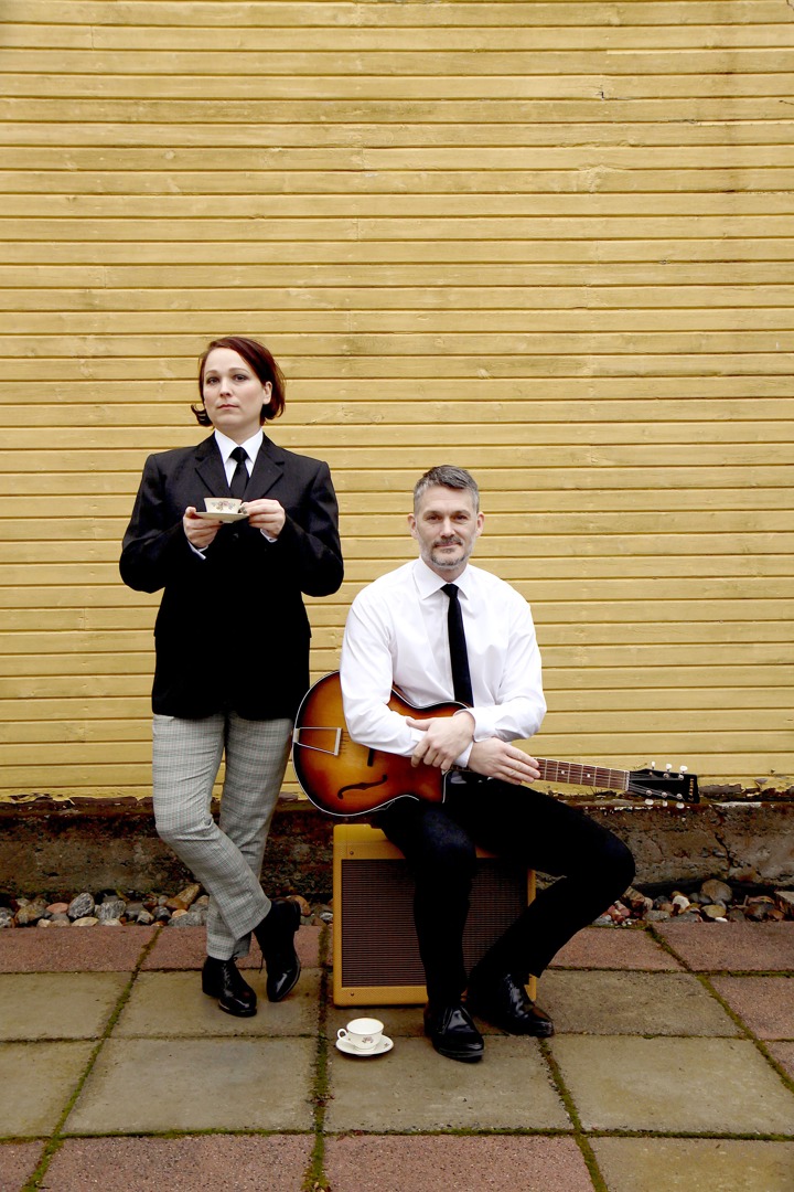 Två musiker iklädd Beatles kostym poserar med gitarr och tekopp