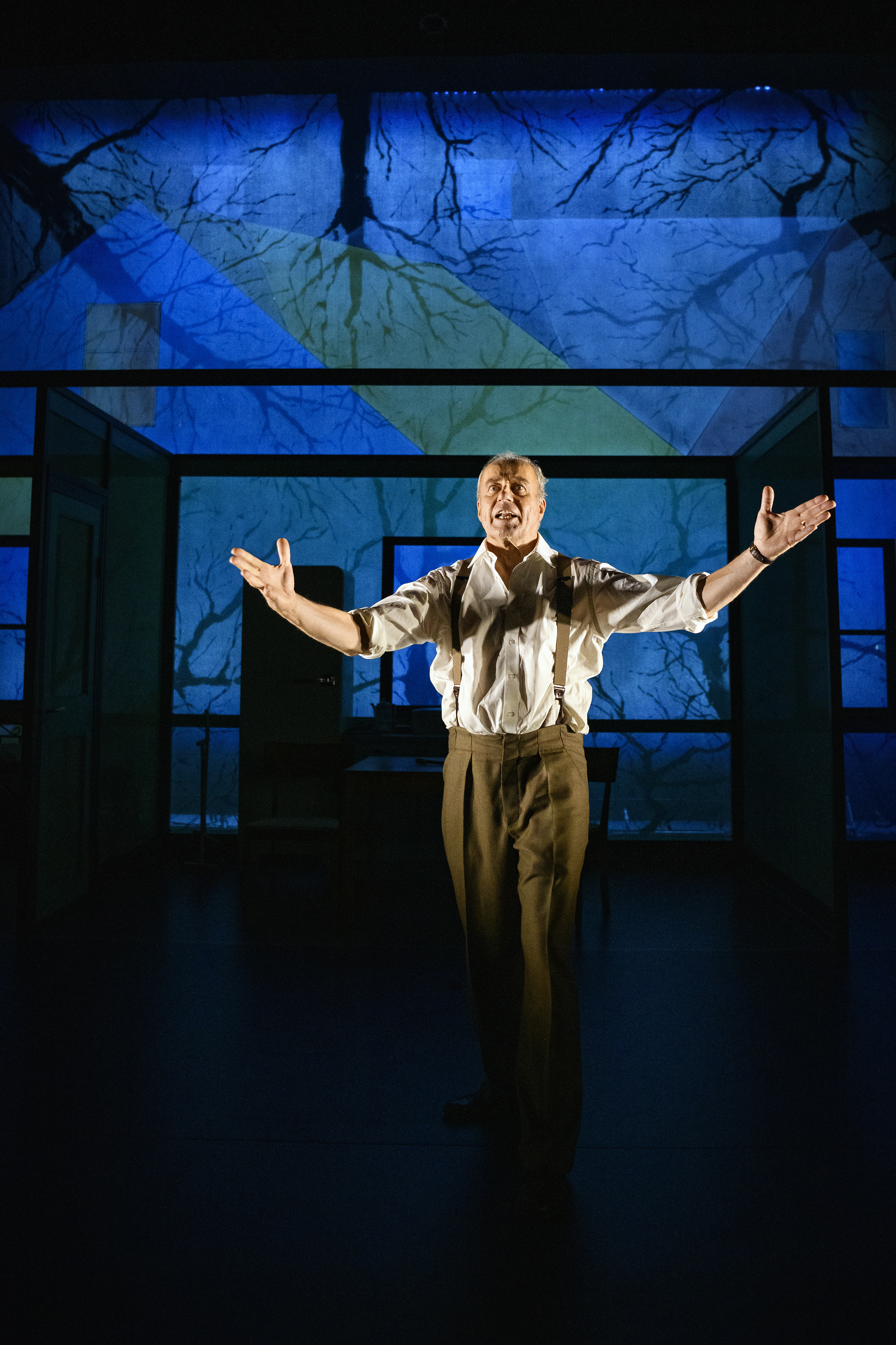 Föreställningsbild från Teater Västernorrlands uppsättning av En handelsresandes död med Lennart Jäkel. Man håller tal på scen i dramatisk belysning.