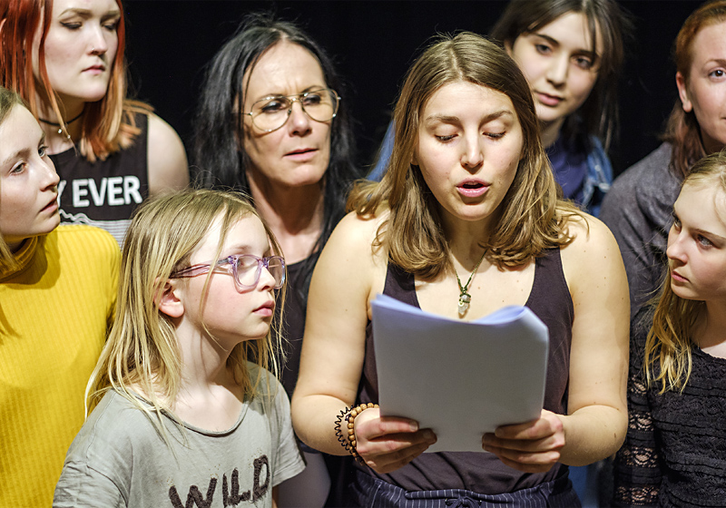 En grupp i olika åldrar läser manus och spelar teater.