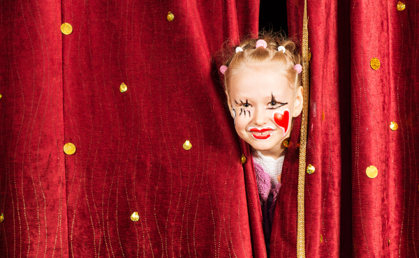 Affischbild för Familjedag på Teater Västernorrland. Ung flicka kikar fram genom en röd ridå.