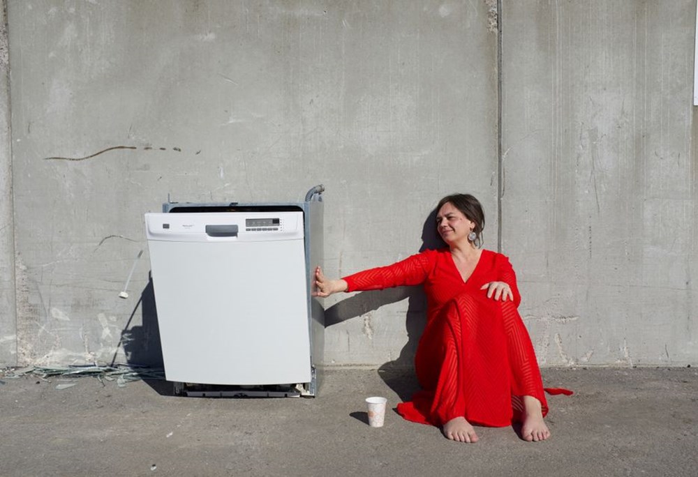 Estradpoeten Ingela Wall sitter mot betong vägg och tar längtansfullt i en diskmaskin.