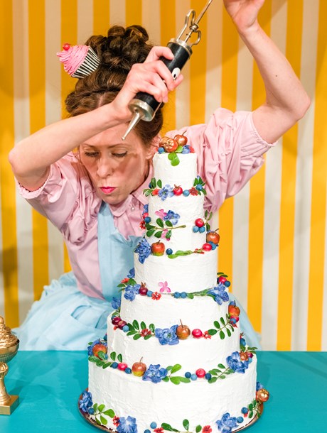 Kvinna i kitschig kostym dekorerar en tårta med många lager